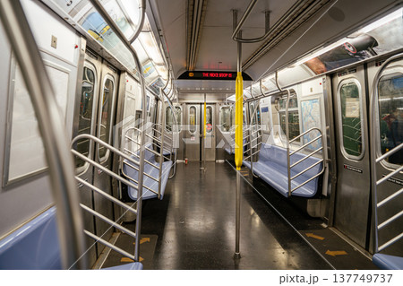 Empty New York City subway train interior showing digital next stop sign and stainless steel doors. Urban public transportation environment with yellow poles, blue seats, and modern metro design. 137749737