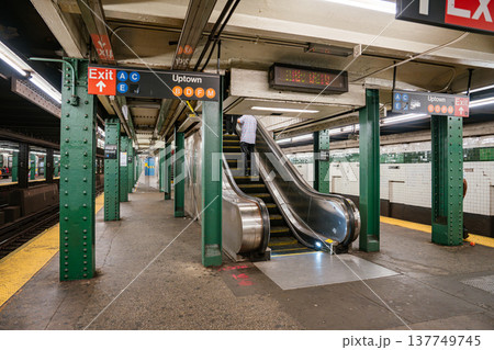 Interior of New York City subway station showing escalator, exit signs, and Uptown train directions at West 4 Street Washington Square. Urban underground transportation hub with green steel columns Interior of New York City subway station showing escalator, exit signs, and Uptown train directions at West 4 Street Washington Square. Urban underground transportation hub with green steel columns 137749745