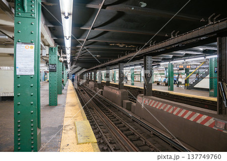 Subway tracks run through West 4 Street station in Manhattan. Green steel columns and yellow platform edge highlight New York City public transportation infrastructure. 137749760