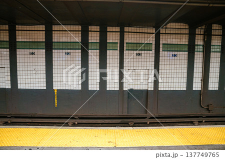 The tiled wall of the 23 Street subway platform is visible inside a Manhattan station. Yellow safety edge and train tracks highlight New York City public transportation infrastructure. The tiled wall of the 23 Street subway platform is visible inside a Manhattan station. Yellow safety edge and train tracks highlight New York City public transportation infrastructure. 137749765
