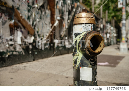 An old fire hydrant stands on a Manhattan sidewalk with peeling posters behind it. The gritty street scene captures authentic New York urban life. 137749768