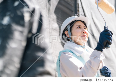 外壁塗装リフォーム。空調服を着用してローラーで丁寧に壁を塗る女性職人 137749773