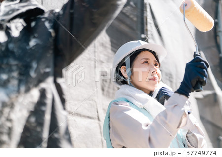 外壁塗装リフォーム。空調服を着用してローラーで丁寧に壁を塗る女性職人 外壁塗装リフォーム。空調服を着用してローラーで丁寧に壁を塗る女性職人 137749774