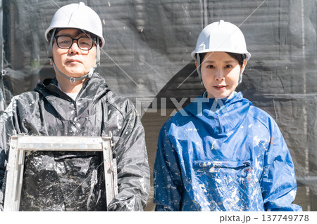 信頼の技術。外壁塗装の現場で共に働くベテランと若手の男女職人 信頼の技術。外壁塗装の現場で共に働くベテランと若手の男女職人 137749778