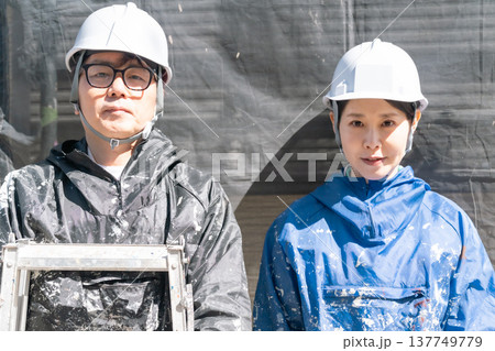 信頼の技術。外壁塗装の現場で共に働くベテランと若手の男女職人 信頼の技術。外壁塗装の現場で共に働くベテランと若手の男女職人 137749779