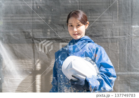 建設業界で活躍する女性職人。ペンキの付いた作業着で微笑む女性塗装工 建設業界で活躍する女性職人。ペンキの付いた作業着で微笑む女性塗装工 137749783