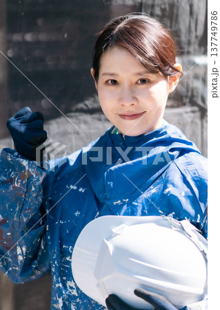 建設業界で活躍する女性職人。ペンキの付いた作業着で微笑む女性塗装工 建設業界で活躍する女性職人。ペンキの付いた作業着で微笑む女性塗装工 137749786