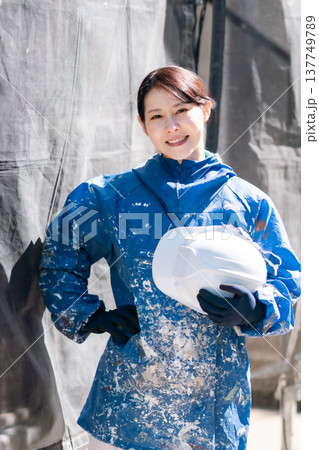 建設業界で活躍する女性職人。ペンキの付いた作業着で微笑む女性塗装工 建設業界で活躍する女性職人。ペンキの付いた作業着で微笑む女性塗装工 137749789