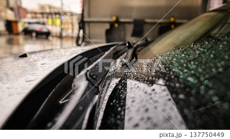Close-up of wet windshield wipers on a dark vehicle during rain at a car wash or street Close-up of wet windshield wipers on a dark vehicle during rain at a car wash or street 137750449