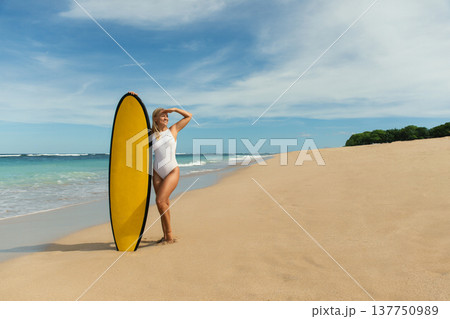 Surfer poses on a beautiful beach with golden sand and calm waves Surfer poses on a beautiful beach with golden sand and calm waves 137750989