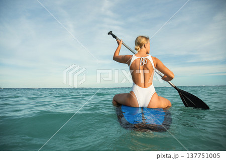 A person paddleboards in calm waters under a bright sky A person paddleboards in calm waters under a bright sky 137751005