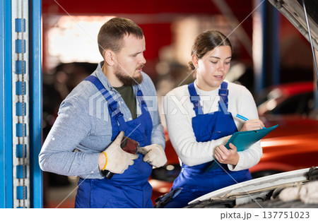 Car service manager discusses car repair problems with mechanic. He takes notes on paper 137751023
