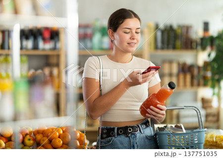 European young woman customer at shop scans QR code on grapefruit juice bottle using phone camera 137751035