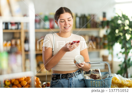 European girl customer at shop scans QR code on tin cans of preserves using phone camera European girl customer at shop scans QR code on tin cans of preserves using phone camera 137751052