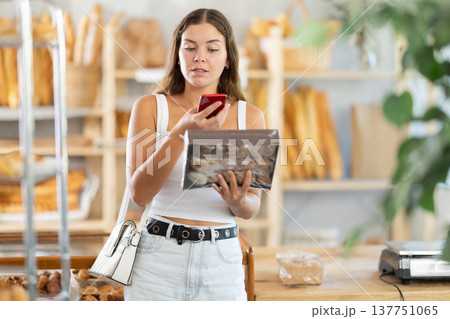 Interested young girl carefully scans a cookie box with her phone Interested young girl carefully scans a cookie box with her phone 137751065