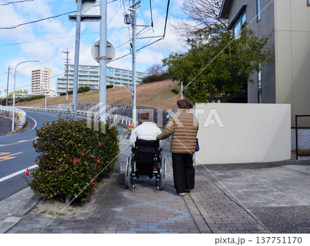 冬の住宅街の道で車椅子を乗る中年障害者と歩く介護する人の姿 冬の住宅街の道で車椅子を乗る中年障害者と歩く介護する人の姿 137751170