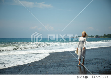 Woman strolls on a black sand beach near the ocean Woman strolls on a black sand beach near the ocean 137751273