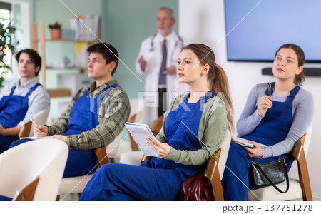 Young female student worker listening to lecture with medical professor in background Young female student worker listening to lecture with medical professor in background 137751278