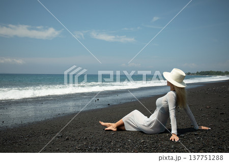 Woman enjoys the sun on a sandy beach near the waves Woman enjoys the sun on a sandy beach near the waves 137751288