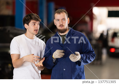 guy talks to a car service mechanic about car repairs guy talks to a car service mechanic about car repairs 137751305