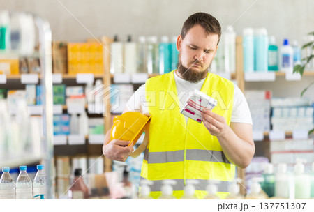 Young man builder chooses paracetamol at pharmacy Young man builder chooses paracetamol at pharmacy 137751307