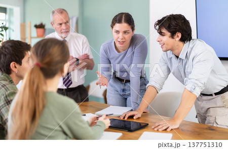 Young students discussing a topic around table monitored by senior teacher 137751310