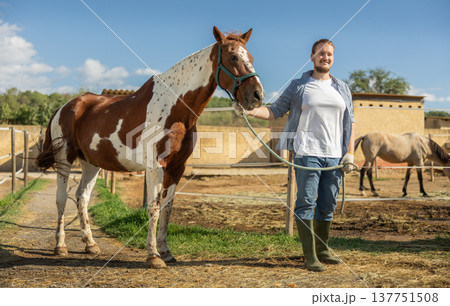 Happy man leading horse by bridle for walk in pasture Happy man leading horse by bridle for walk in pasture 137751508