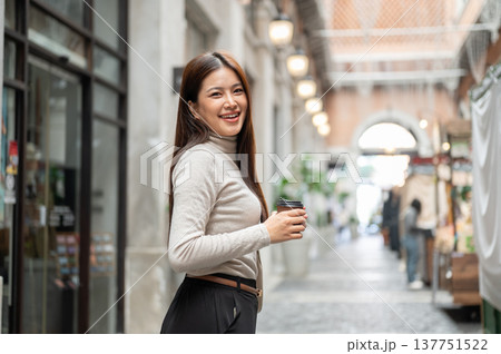 Happy asian woman holding coffee cup while walking or standing sideway in a shopping mall or market. Happy asian woman holding coffee cup while walking or standing sideway in a shopping mall or market. 137751522