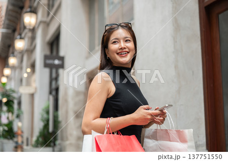 Pretty asian woman holding phone and shopping bags walking or standing sideway in a mall or market. Pretty asian woman holding phone and shopping bags walking or standing sideway in a mall or market. 137751550