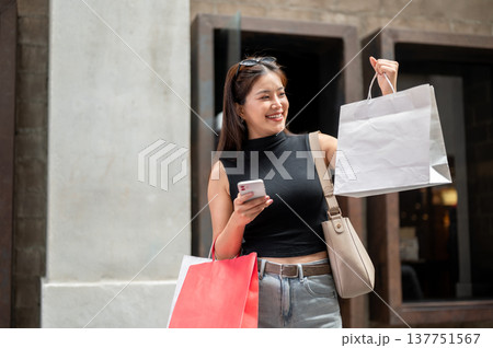Pretty asian woman holding phone looking at shopping bag while walking or standing in mall or market Pretty asian woman holding phone looking at shopping bag while walking or standing in mall or market 137751567