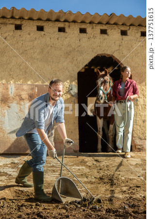 Young man cleans manure near stable Young man cleans manure near stable 137751615