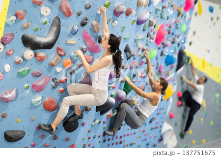 Motivated young girl climbing without ropes and harnesses on artificial bouldering wall in fitness center 137751675
