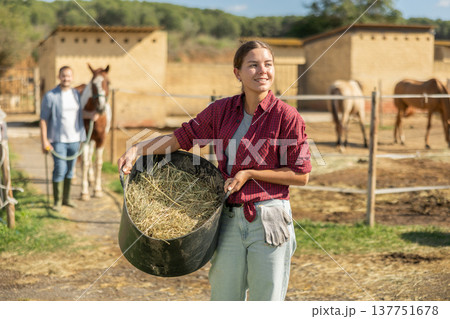 Young woman with bucket of hay feed for horse 137751678