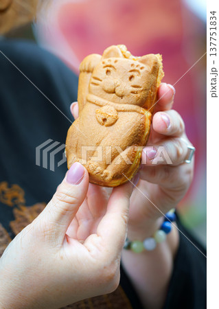 Tokyo, Japan - Sep 30 2024, vertical view of a taiyaki pie in the shape of a Maneki Neko cat, which is held in the hands of a man, at daytime, Tokyo, Japan 137751834