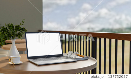 White screen laptop and coffee cup with eyeglasses over book on round wooden table at cafe balcony. White screen laptop and coffee cup with eyeglasses over book on round wooden table at cafe balcony. 137752037