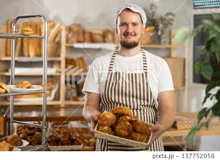 Male seller holds basket with finished products, shows many croissants 137752058