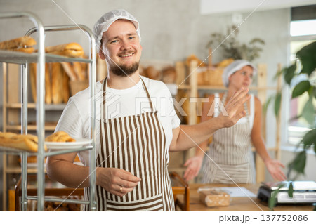 Content young man worker stands with his back to frustrated girl behind bakery counter Content young man worker stands with his back to frustrated girl behind bakery counter 137752086