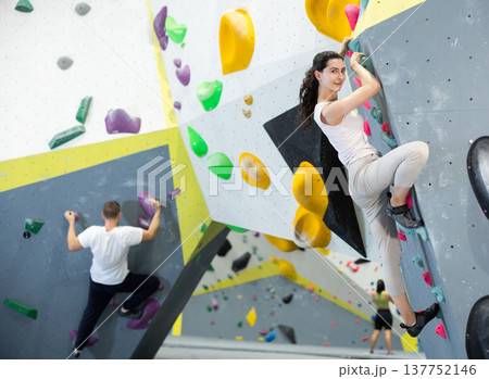 Motivated young girl climbing without ropes and harnesses on artificial bouldering wall in fitness center Motivated young girl climbing without ropes and harnesses on artificial bouldering wall in fitness center 137752146