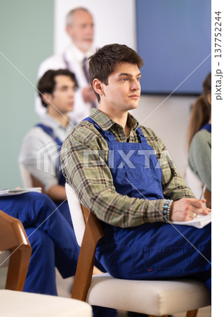 Young guy in blue overalls watching presentation with a doctor standing in background 137752244