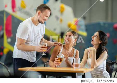 Man and two girls meet after rock climbing training - discussing successes and failures together at table, chatting and drinking beer Man and two girls meet after rock climbing training - discussing successes and failures together at table, chatting and drinking beer 137752263