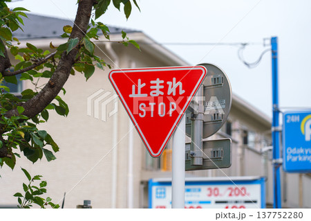 Tokyo, Japan - Sep 30 2024, A close-up view of a triangular red traffic stop sign hanging over the road, with building facades and an cloudy sky in the background, Tokyo, Japan 137752280