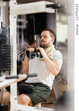 Man in gym performs exercises for arm muscles using cable crossover machine and pull weighted rope Man in gym performs exercises for arm muscles using cable crossover machine and pull weighted rope 137752423