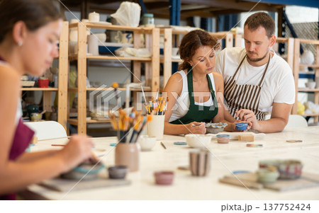 During master class, student paints clay vessel under guidance of male teacher. During master class, student paints clay vessel under guidance of male teacher. 137752424