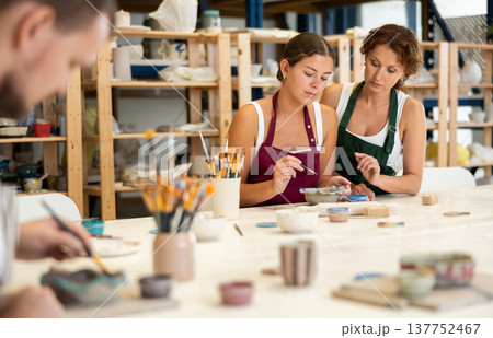 During master class, student paints clay vessel under guidance of female teacher. 137752467