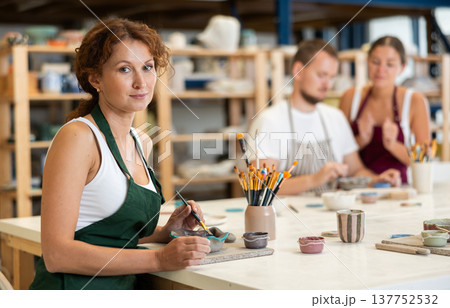 During workshop at master class, female employee paints clay vessel plate 137752532