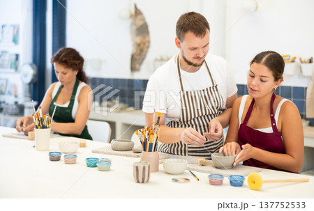 Pupils are sitting near work table, sculpting plate of raw clay under supervision of male teacher 137752533
