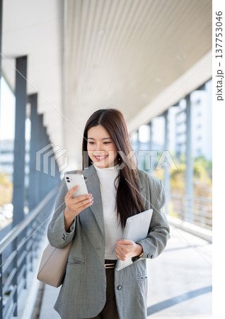 Pretty asian woman student office worker holding tablet looking at phone while walking on footbridge 137753046