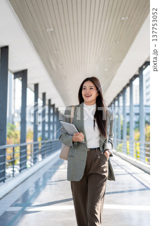 Smart asian woman student office worker holding tablet putting hand in pocket walking on footbridge. 137753052