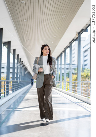 Full body asian woman student office worker holding tablet walking with hand in pocket on footbridge 137753053