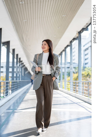 Happy asian woman student office worker holding tablet and walking with hand in pocket on footbridge 137753054